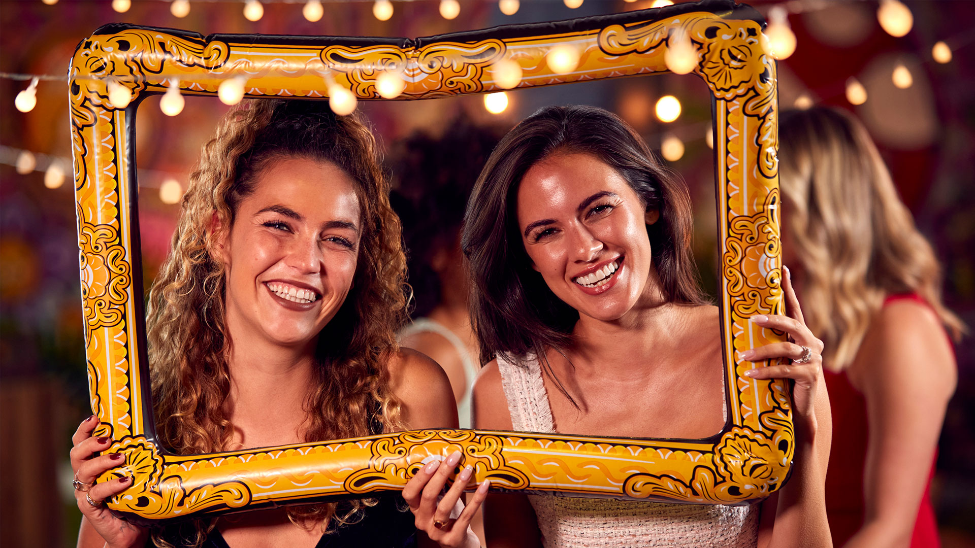 two attractive young women pose for a photo while holding a picture frame prop